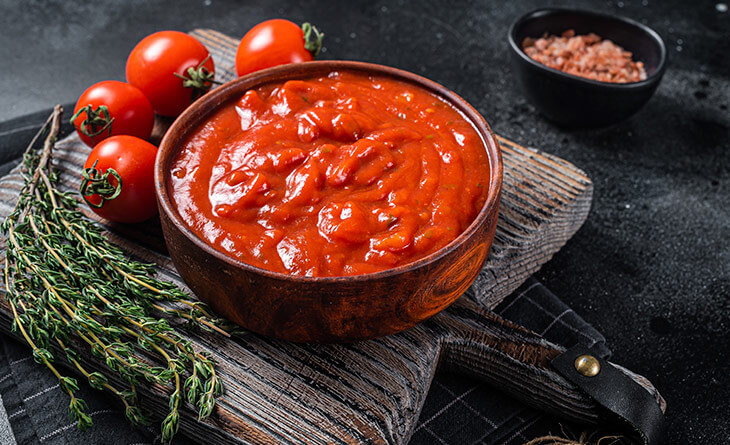 O segredo do nosso molho de tomate caseiro- Molho de tomate caseiro servido em pote de vidro, com ervas frescas ao fundo